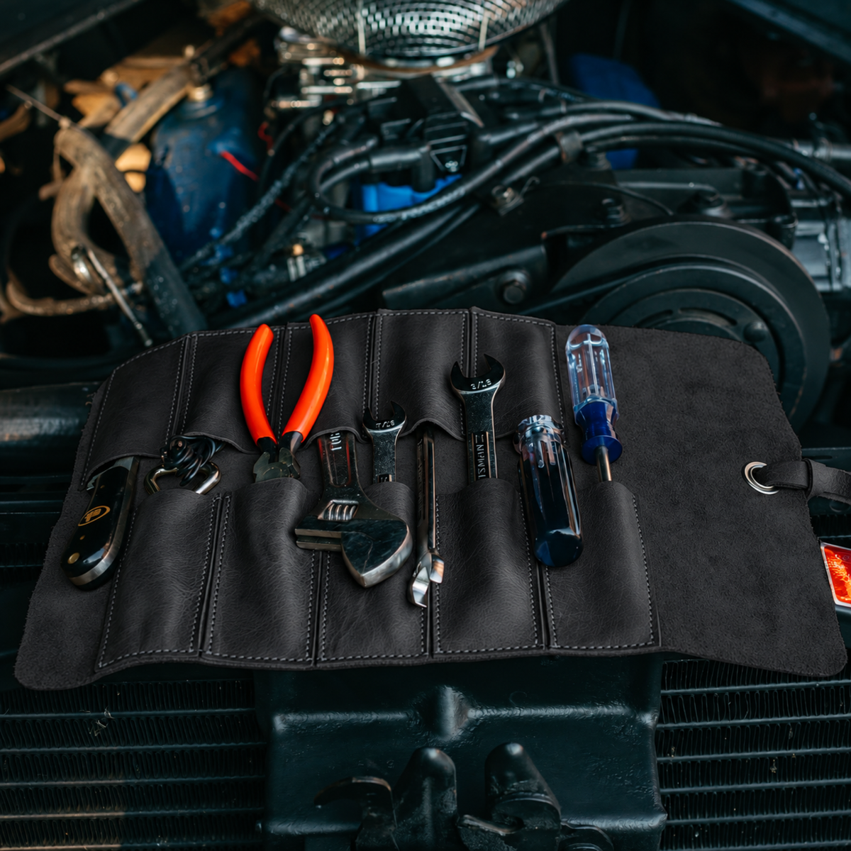 Black leather tool roll with tools across an engine